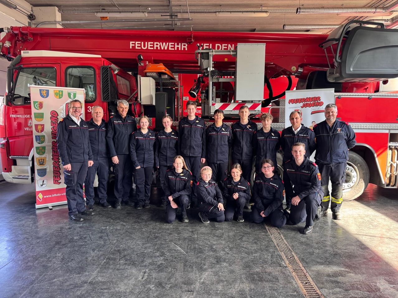 Eine Gruppe Feuerwehrleute in Uniformen steht vor einem roten Feuerwehrauto mit der Aufschrift 'Feuerwehr Felden'. Einige knien, andere stehen. Sie scheinen für ein Foto zu posieren.