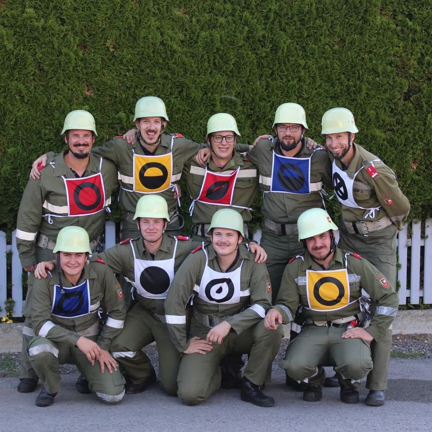 Eine Gruppe von Männern in Militäruniformen posiert für ein Foto mit Helmen, lächelt und einige stehen hintereinander.