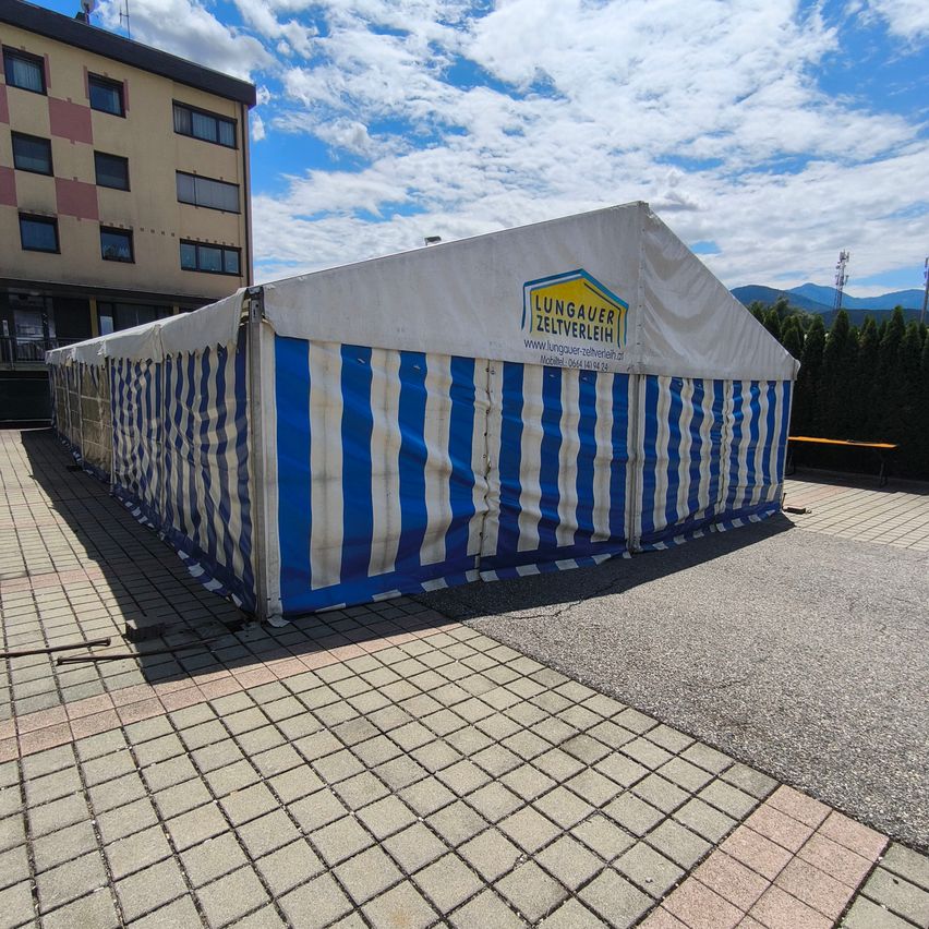 A large blue and white striped tent is set up on a paved area, with a building in the background.