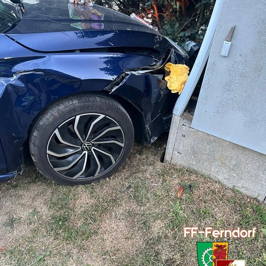 A blue car has collided with a concrete pillar, causing damage to the front bumper and fender. A yellow cloth is draped over the damaged area.