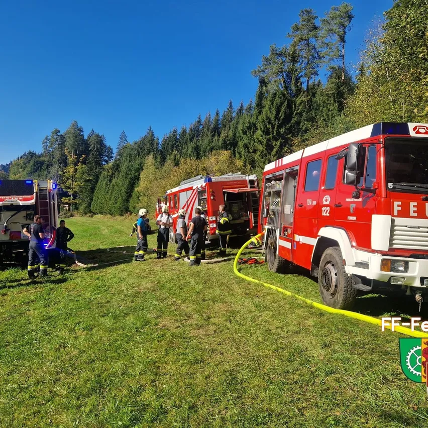 Eine Gruppe von Feuerwehrleuten steht um einen Feuerwehrwagen auf einem Rasenfeld.