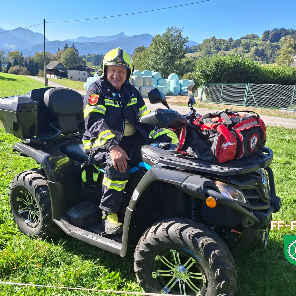 Ein Feuerwehrmann sitzt auf einem vierrädrigen Fahrzeug in einem Grasfeld.
