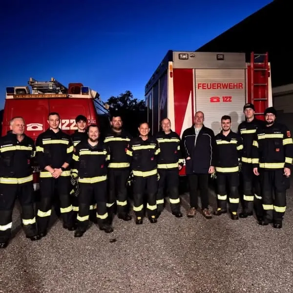 Eine Gruppe von Feuerwehrleuten in Uniform posiert für ein Foto vor ihren Feuerwehrwagen.