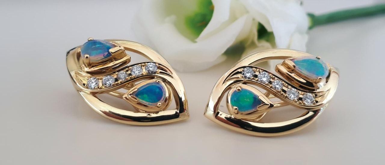 Zwei goldfarbene Ohrringe mit Opal- und Diamantsteinen, die auf einem weißen Hintergrund liegen.