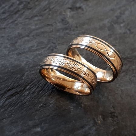 Zwei goldene Ringe mit schwarzen und weißen Blumendesigns auf einer dunklen Oberfläche.