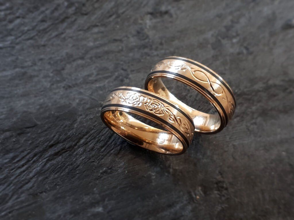 Zwei goldene Ringe mit schwarzen und weißen Blumendesigns auf einer dunklen Oberfläche.