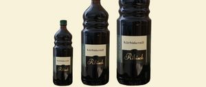Drei Flaschen Ribisel schwarzer Johannisbeersaft mit grünen Verschlüssen, auf gelbem Hintergrund präsentiert.