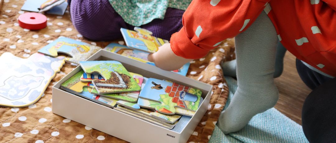 Zwei Kinder spielen mit einer Puzzle-Box, eines im roten Shirt und das andere im grünen Kleid.
