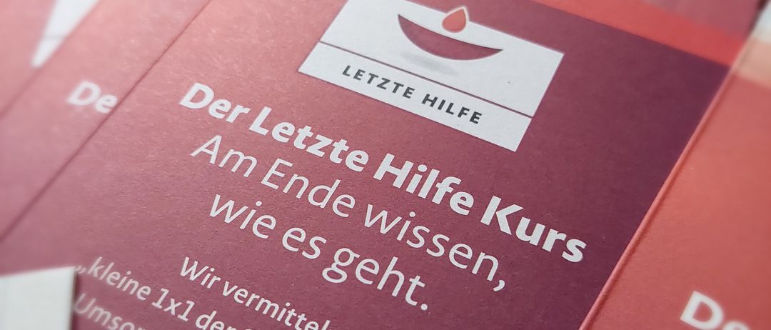 Eine Broschüre mit dem Titel 'Der Letzte Hilfe Kurs' ist prominent ausgestellt. Sie konzentriert sich auf die Bereitstellung von Anleitung für die Sterbebegleitung.