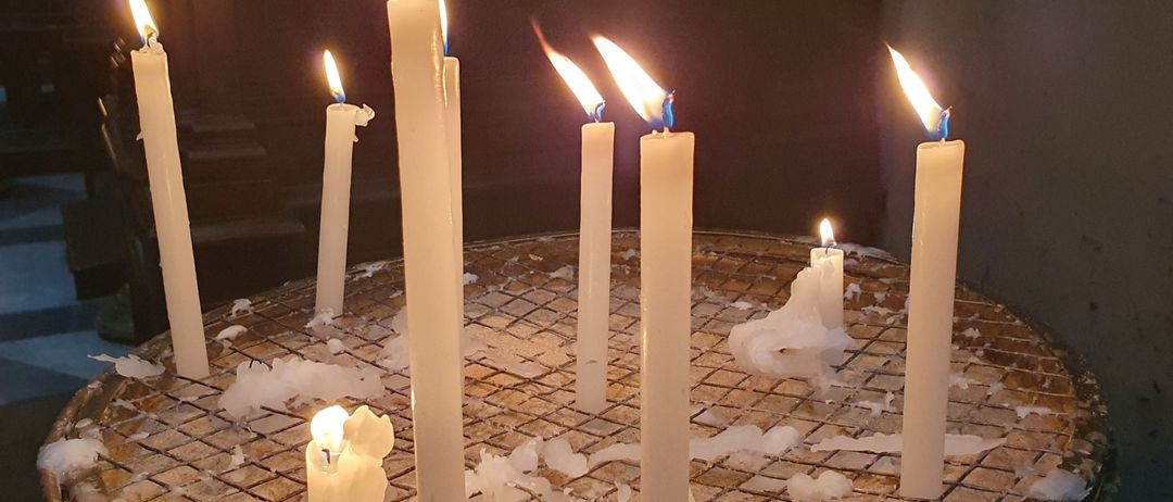 Mehrere weiße Kerzen sind entzündet und in einer kreisförmigen Anordnung auf einer gefliesten Oberfläche platziert, mit geschmolzenem Wachs darum herum.