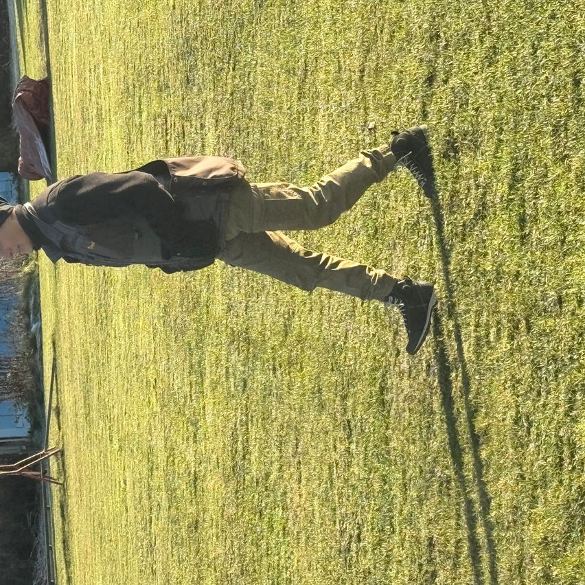 Eine Person mit Rucksack liegt auf einem grünen Rasenfeld mit verwischtem Hintergrund.