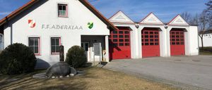 Ein weißes Gebäude mit rotem Rand hat F.F. Aderklaa Text über dem Eingang. Drei rote Garagen sind an das Gebäude angebaut.