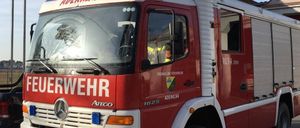 Ein roter und weißer Feuerwehrwagen mit der Aufschrift 'Feuerwehr' steht vor einem Gebäude. Der Wagen hat ein Nummernschild mit der Aufschrift 'GF 935 BC'.