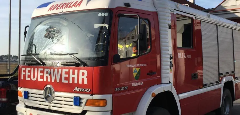 Ein roter und weißer Feuerwehrwagen mit der Aufschrift 'Feuerwehr' steht vor einem Gebäude. Der Wagen hat ein Nummernschild mit der Aufschrift 'GF 935 BC'.