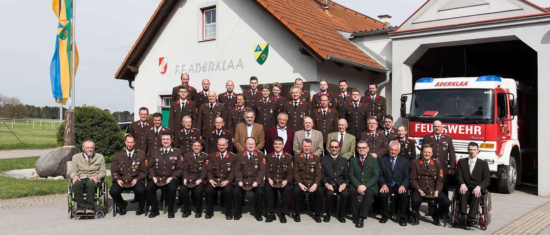 Eine Gruppe von Männern in Militäruniformen posiert für ein Foto vor einem Gebäude, vor dem ein Feuerwehrwagen geparkt ist.
