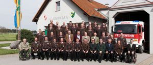A group of men in military uniforms posing for a photo in front of a building with a fire truck parked in front.