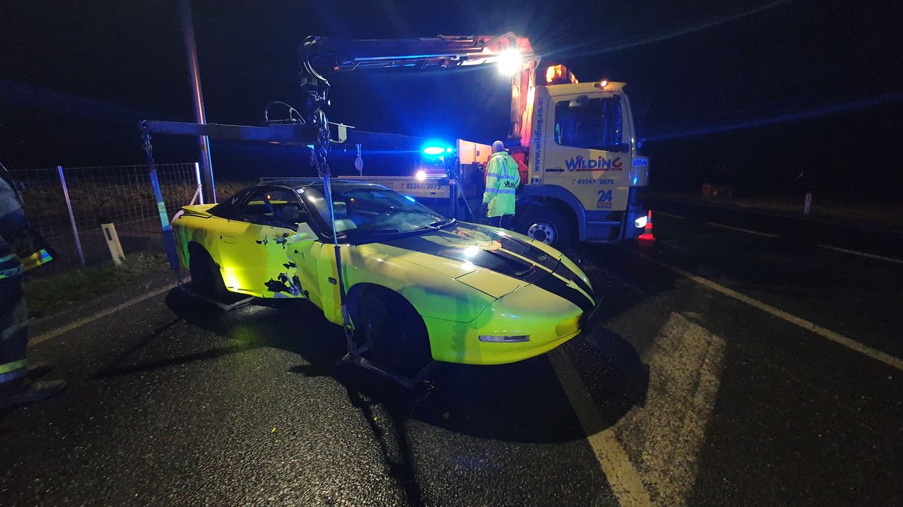 Ein gelber Sportwagen wird bei Nacht von einem Kran angehoben, mit blinkenden Polizeilichtern im Hintergrund.