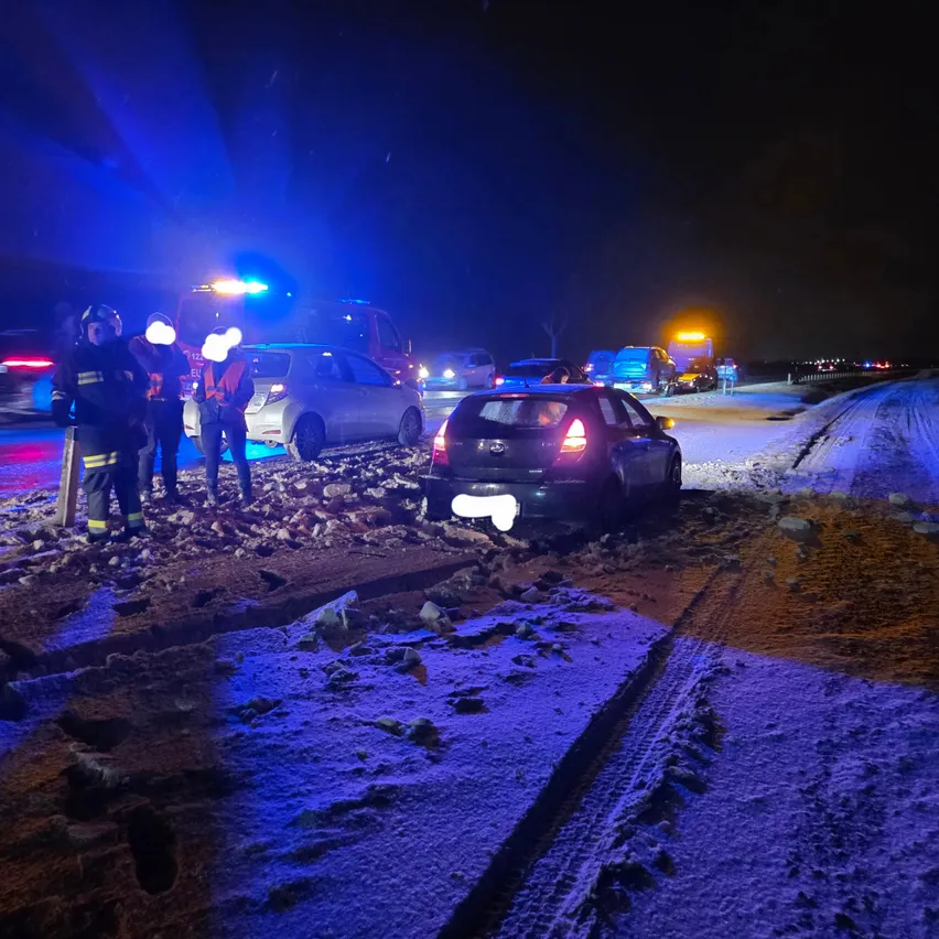 Rettungsfahrzeuge und Feuerwehrleute sind am Unfallort eines Autounfalls auf einer verschneiten Straße bei Nacht.