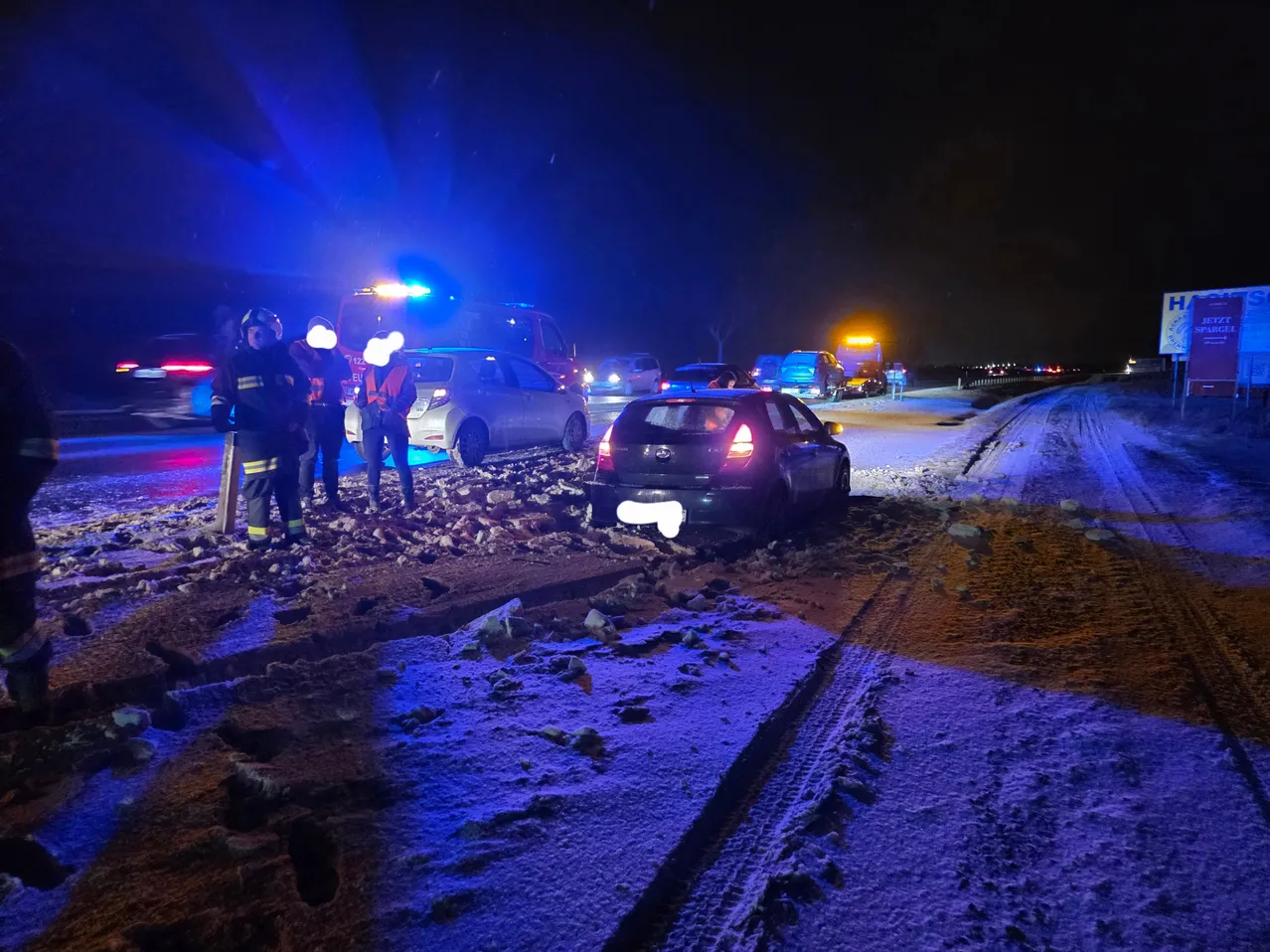 Rettungsfahrzeuge und Feuerwehrleute sind am Unfallort eines Autounfalls auf einer verschneiten Straße bei Nacht.