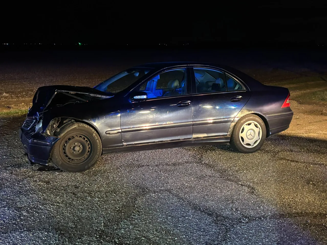 Ein schwarzer Mercedes-Benz ist nachts auf einem Schotterweg geparkt, mit beschädigter Front.