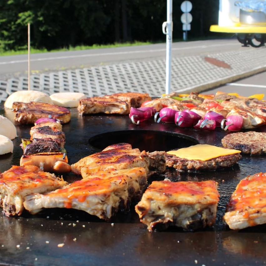 Ein großer Grilltisch mit verschiedenen gegrillten Fleischsorten, Gemüse und Käse, im Freien aufgestellt.