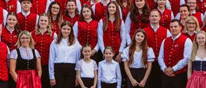 Ein Chor in roten Westen und schwarzen Hosen posiert für ein Gruppenfoto auf einer Treppe. Der Chor besteht aus Erwachsenen und Kindern, und alle lächeln.