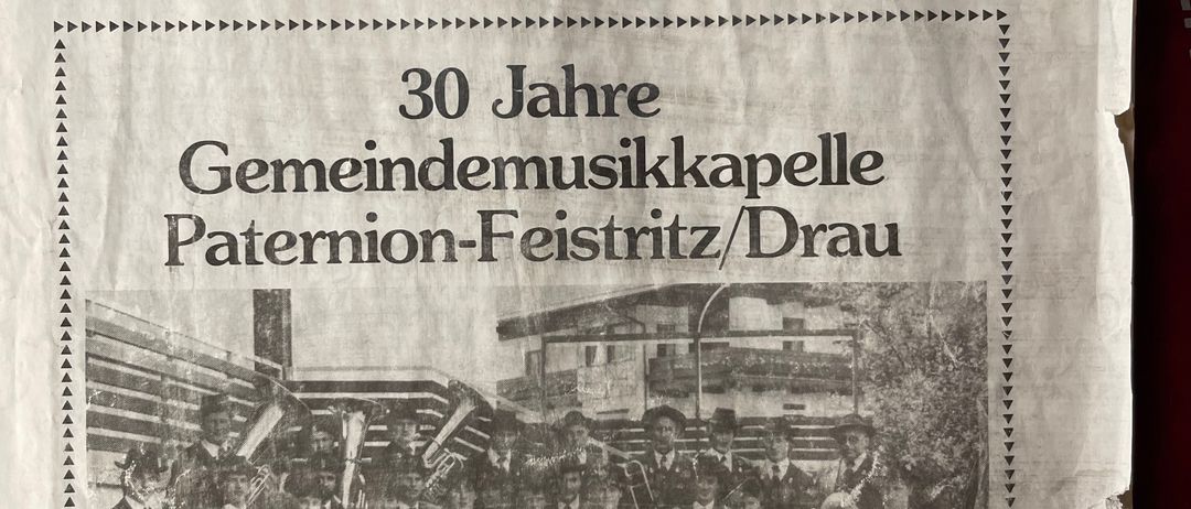 Ein Schwarz-Weiß-Foto einer Blaskapelle mit Mitgliedern in Uniformen und Hüten steht vor einem Gebäude. Es ist eine Seite aus einer Gemeindezeitung für Paterion-Feistritz/Drau, August 1983.