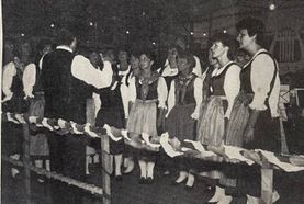 Eine Gruppe von Menschen in traditioneller Kleidung steht in einer Reihe, vielleicht bei einem Fest oder Ereignis. Sie schauen nach oben, möglicherweise in Ehrfurcht.