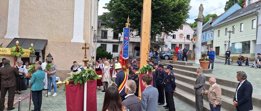 Eine Gruppe von Menschen versammelt sich vor einem Fahnenmast, einige in Uniformen gekleidet. Einige Leute stehen auf den Stufen, während andere aus der Ferne zusehen.