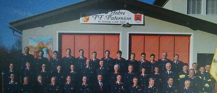 Eine Gruppenaufnahme von Feuerwehrleuten in Uniform vor einem Feuerwehrhaus mit einem Schild, das '125 Jahre FF Paternon' steht.