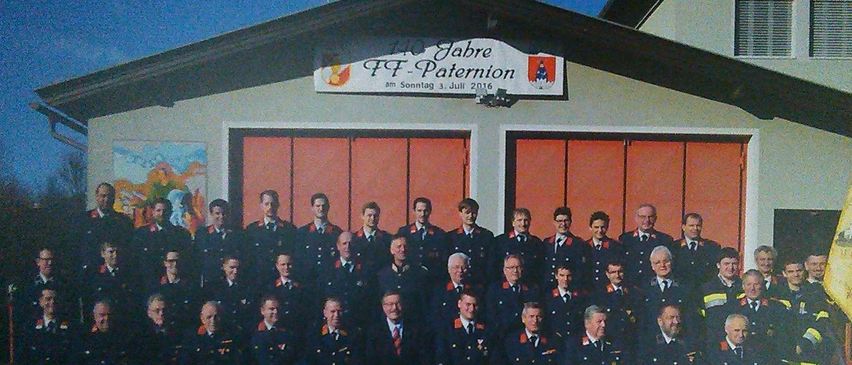 Eine Gruppenaufnahme von Feuerwehrleuten in Uniform vor einem Feuerwehrhaus mit einem Schild, das '125 Jahre FF Paternon' steht.