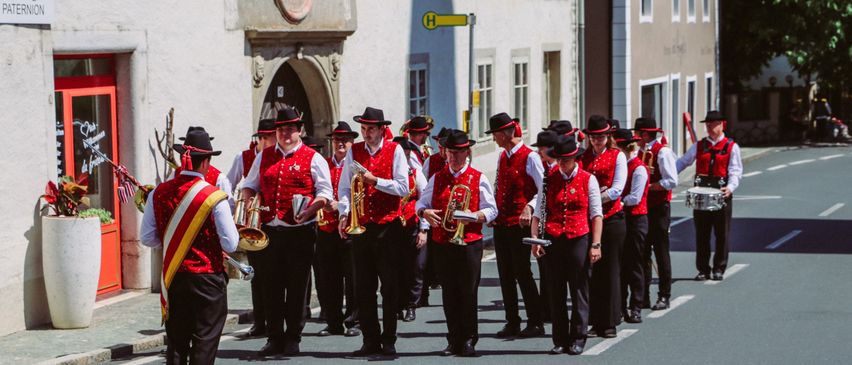Eine Blaskapelle in roten Westen und schwarzen Hüten spielt Trompeten und Trommeln bei einer Parade auf einer Stadtstraße.