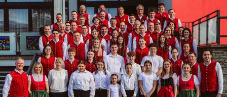 Eine große Gruppe von Menschen in roten Westen und weißen Hemden steht auf den Stufen vor einem Gebäude. Sie posieren für ein Foto.