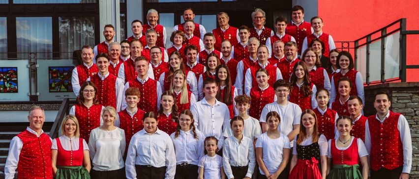 Eine große Gruppe von Menschen in roten Westen und weißen Hemden steht auf den Stufen vor einem Gebäude. Sie posieren für ein Foto.