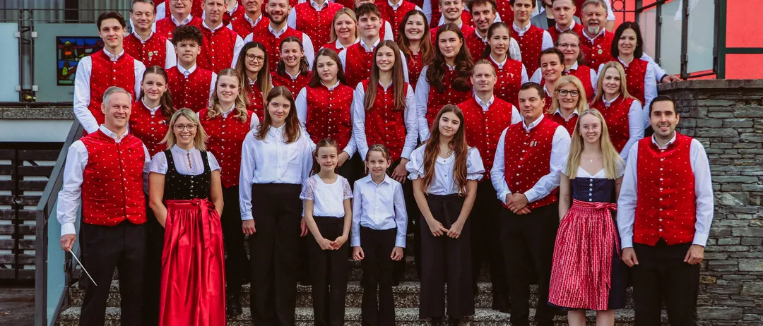 Eine Gruppe von Menschen in roten Westen und weißen Hemden posiert für ein Foto vor einem Gebäude.