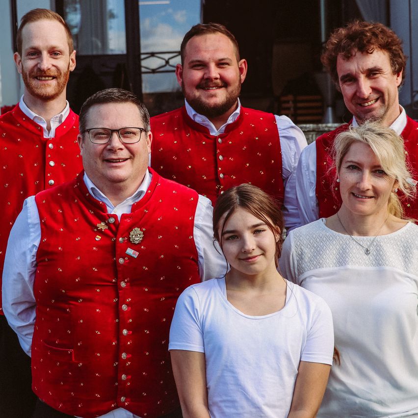 Eine Gruppe von fünf Personen, drei Männer und zwei Frauen, posiert für ein Foto. Sie alle lächeln und scheinen eine gute Zeit zu haben. Die Männer tragen rote Westen mit weißen Hemden, während die Frauen weiße Hemden tragen.