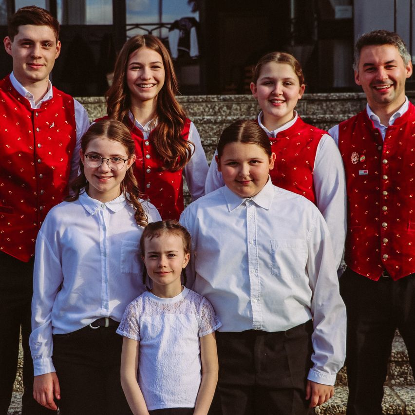 Eine Gruppe junger Menschen in traditioneller Kleidung, die vor einem Gebäude mit lächelndem Gesicht stehen.