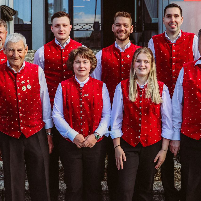 Gruppe von Menschen in roten Westen und weißen Hemden posiert für ein Foto vor einem Gebäude.