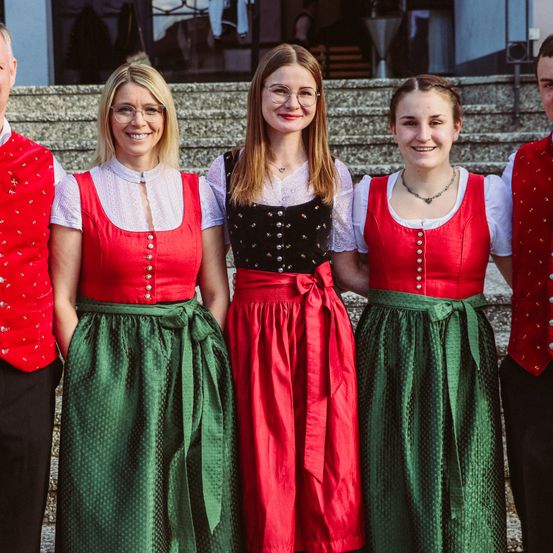 Vier Menschen stehen auf einer Treppe, tragen traditionelle Kleidung, lächeln und posieren für ein Foto.