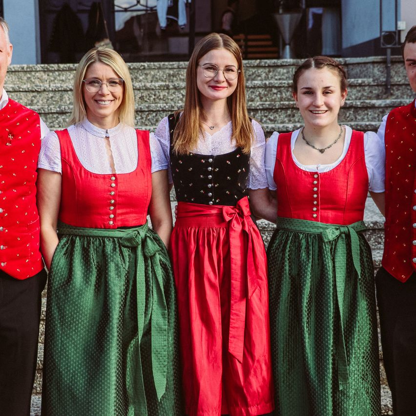 Vier Menschen stehen auf einer Treppe, tragen traditionelle Kleidung, lächeln und posieren für ein Foto.