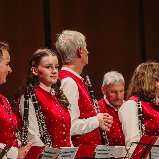 Eine Gruppe von Klarinettisten, die rote Westen mit Musiknoten tragen, stehen in einer Reihe und halten ihre Klarinetten.