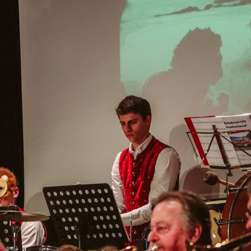 Ein junger Mann spielt ein Blechblasinstrument vor einem Notenständer und einem Schlagzeuger.
