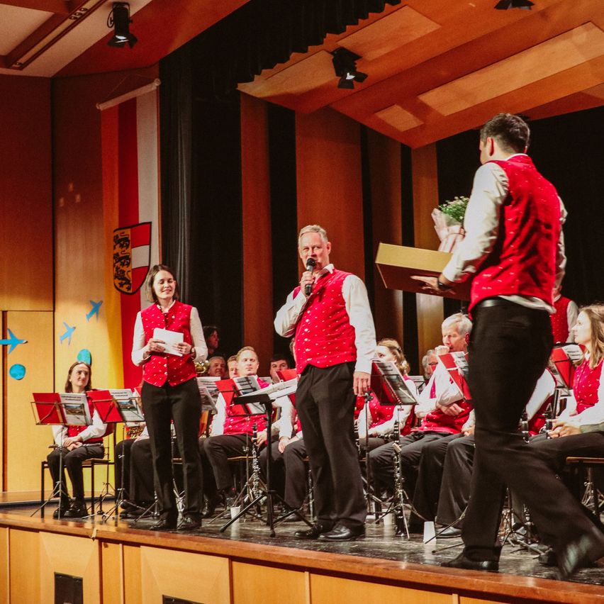 Eine Gruppe von Menschen in roten Westen führt mit Musikinstrumenten auf einer Bühne auf.