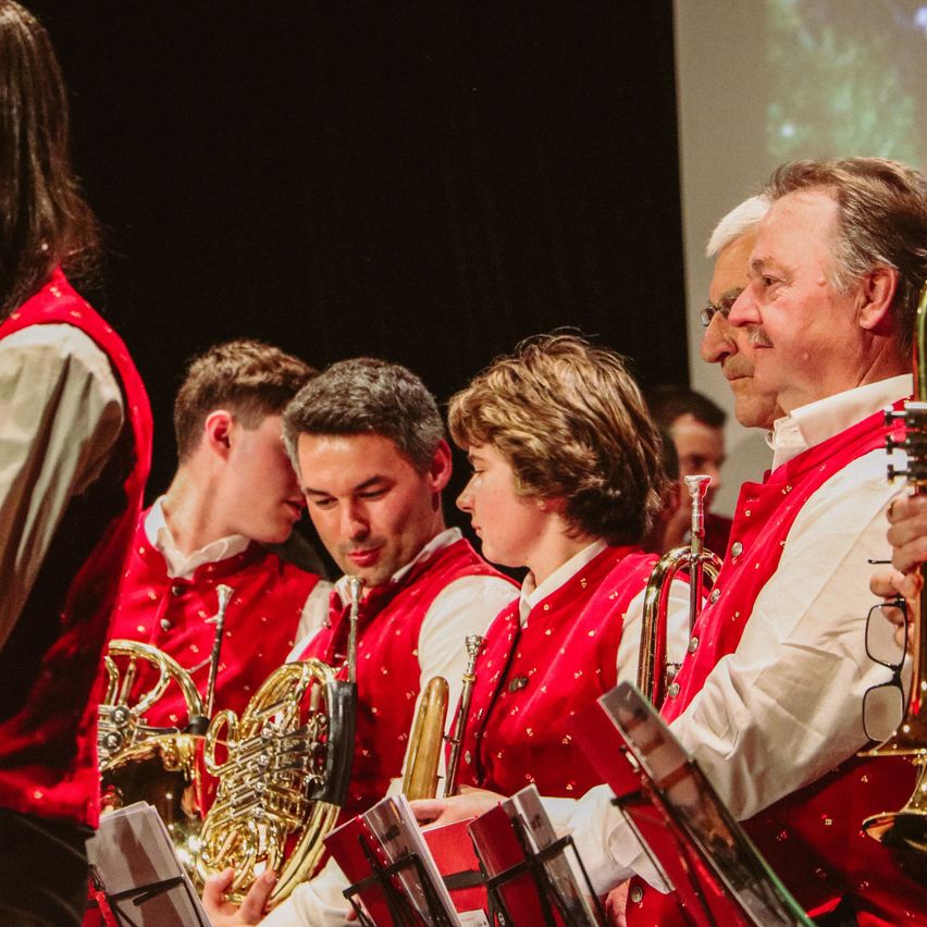 Eine Gruppe von Musikern, die rote Westen mit weißen langen Ärmeln tragen und Musikinstrumente halten.