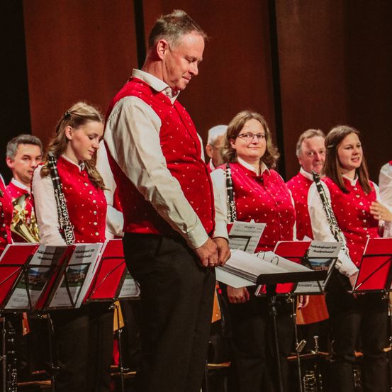 Ein Mann und eine Frau in roten gepunkteten Westen spielen Musikinstrumente auf der Bühne, wobei der Mann ein Musikblatt hält.