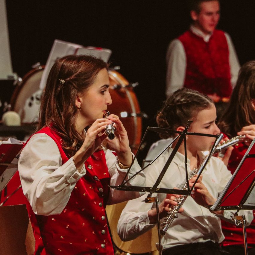 Eine Gruppe junger Musiker, in roten Westen gekleidet, tritt auf der Bühne auf. Die Frau vorne spielt Flöte, während andere Flöte und Trommeln spielen.