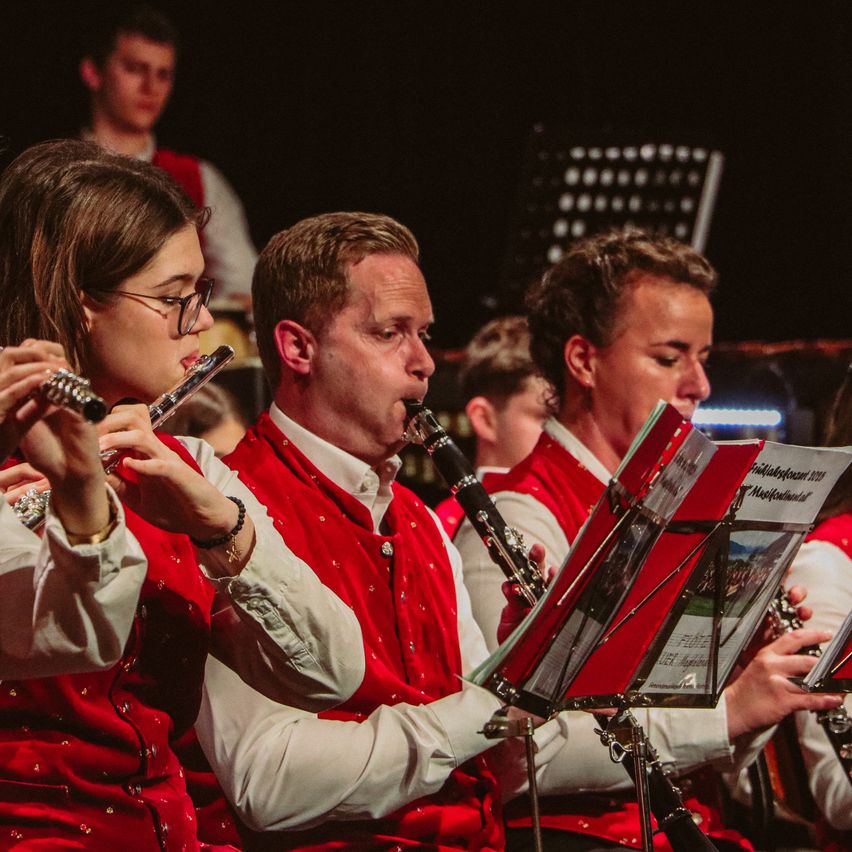 Eine Frau spielt Flöte und ein Mann Klarinette in einer Band mit anderen Bandmitgliedern, alle tragen rote Westen.