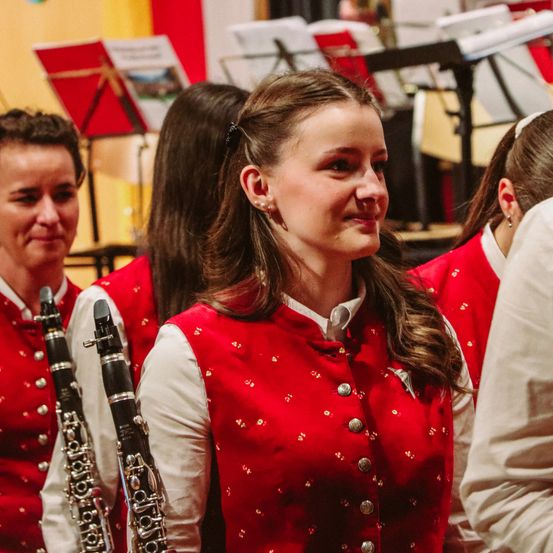 Mehrere Musikerinnen in roten und weißen Uniformen, zwei von ihnen halten eine Klarinette, während andere im Hintergrund verschwommen sind.