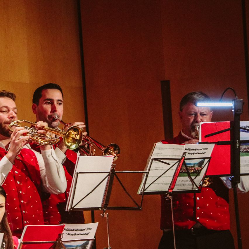 Drei Männer spielen Trompeten auf der Bühne, mit Notenständern vor ihnen und einer Lampe, die einen der Musiker beleuchtet.