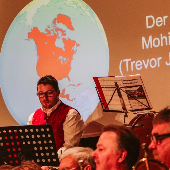 Ein Mann spielt Geige vor einer Projektion einer Karte von Nordamerika und Europa.